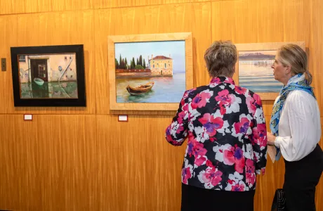 Two alums admiring paintings on the wall in the Alumnae House gallery