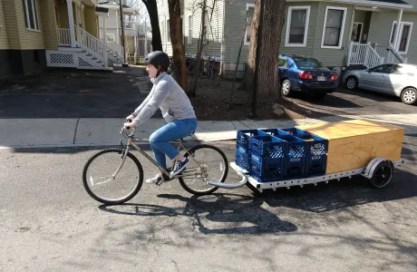 A student pedals a bicycle, pulling the portable ParkKit in tow