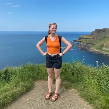 Abi Bowering ’24 squinting and smiling in the sun in front of an ocean vista