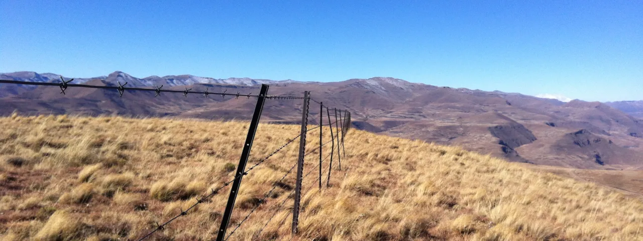 A barbed wire fence across a field with mountains in the background