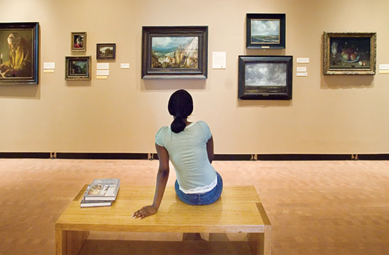 Student on a bench in the museum looking at paintings on the wall