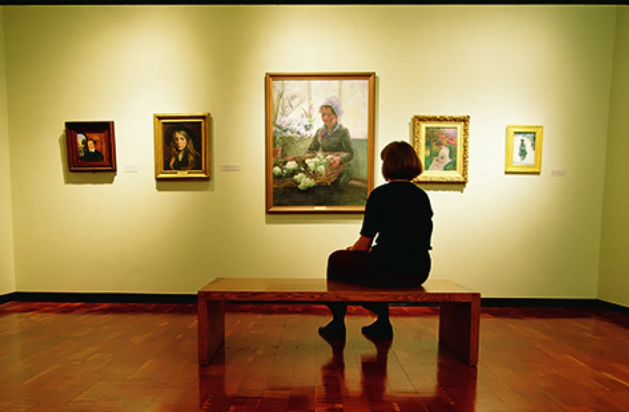 Student sitting on a bench looking at paintings inside the art museum