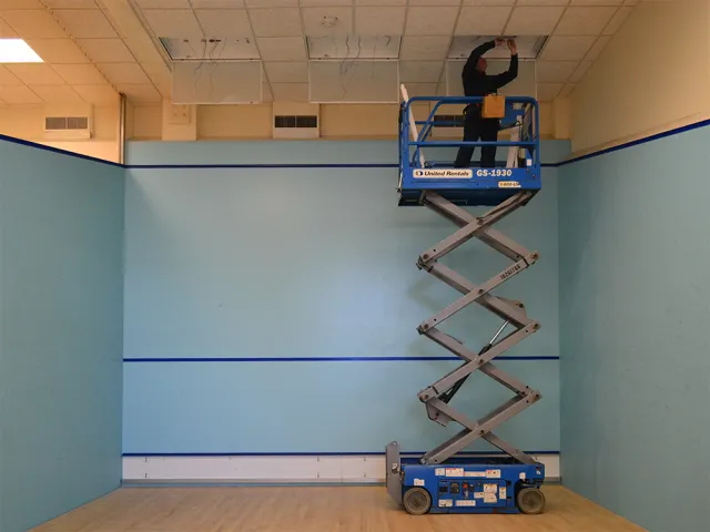 An electrician working on ceiling lighting in the squash courts