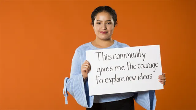 Andrea Botello holding a sign saying This community gives me the courage to explore new ideas