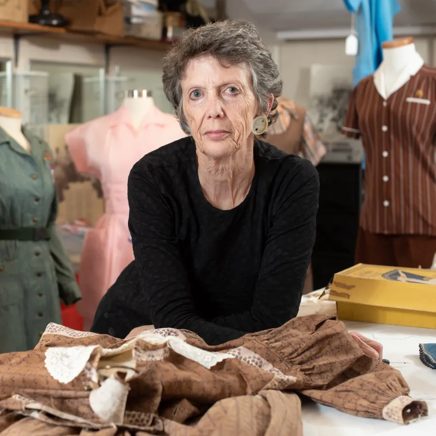 Kiki Smith leans on a table, surrounded by clothing.