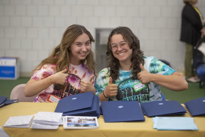 Two students smiling and giving thumbs-ups to the camera.