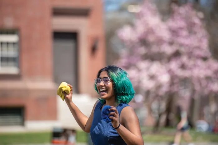 A student smiling and holding bean bags, while playing a lawn game.