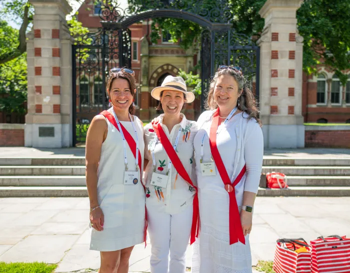 Three alums dressed in white standing in front of the Grecourt Gates