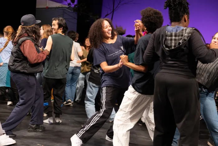 Two students smiling and looking at each other, holding hands as they dance on a stage