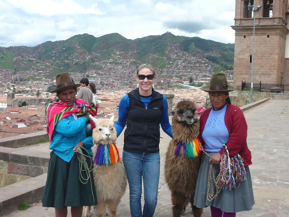 A woman poses with llamas and two Peruvian women
