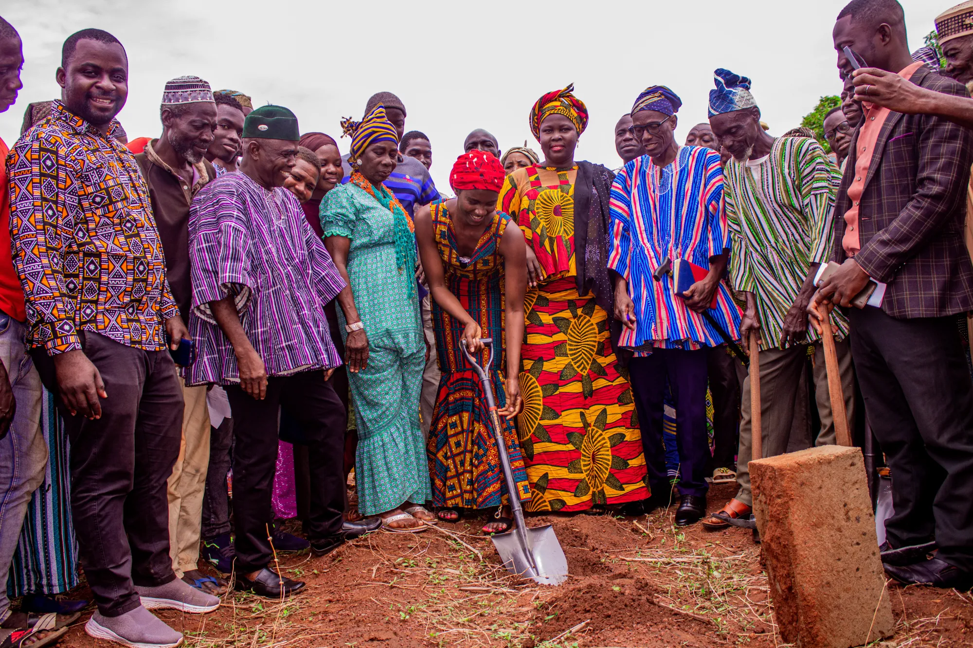 Group of people standing, one of them holding a shovel pointed into the dirt below, breaking ground for the building of the new school.