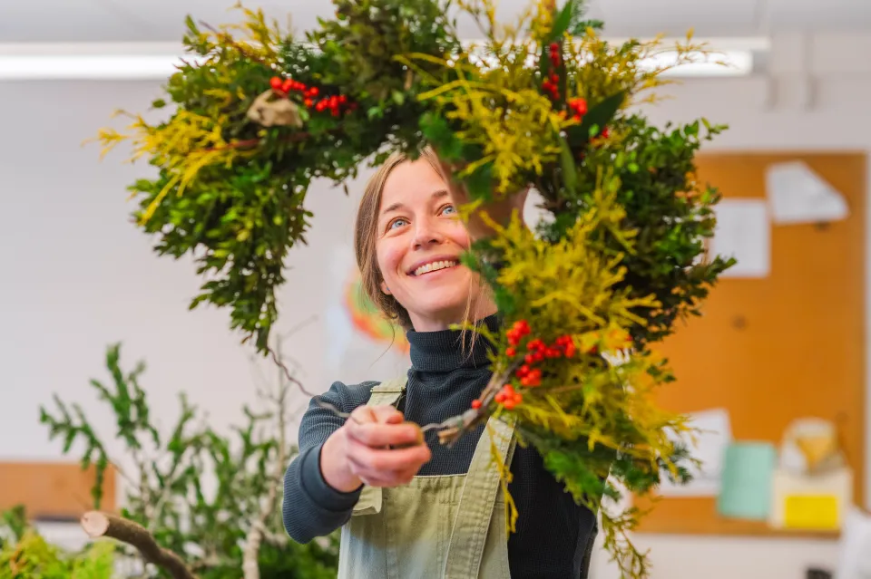 Julie Thomson smiles while holding a half completed wreath