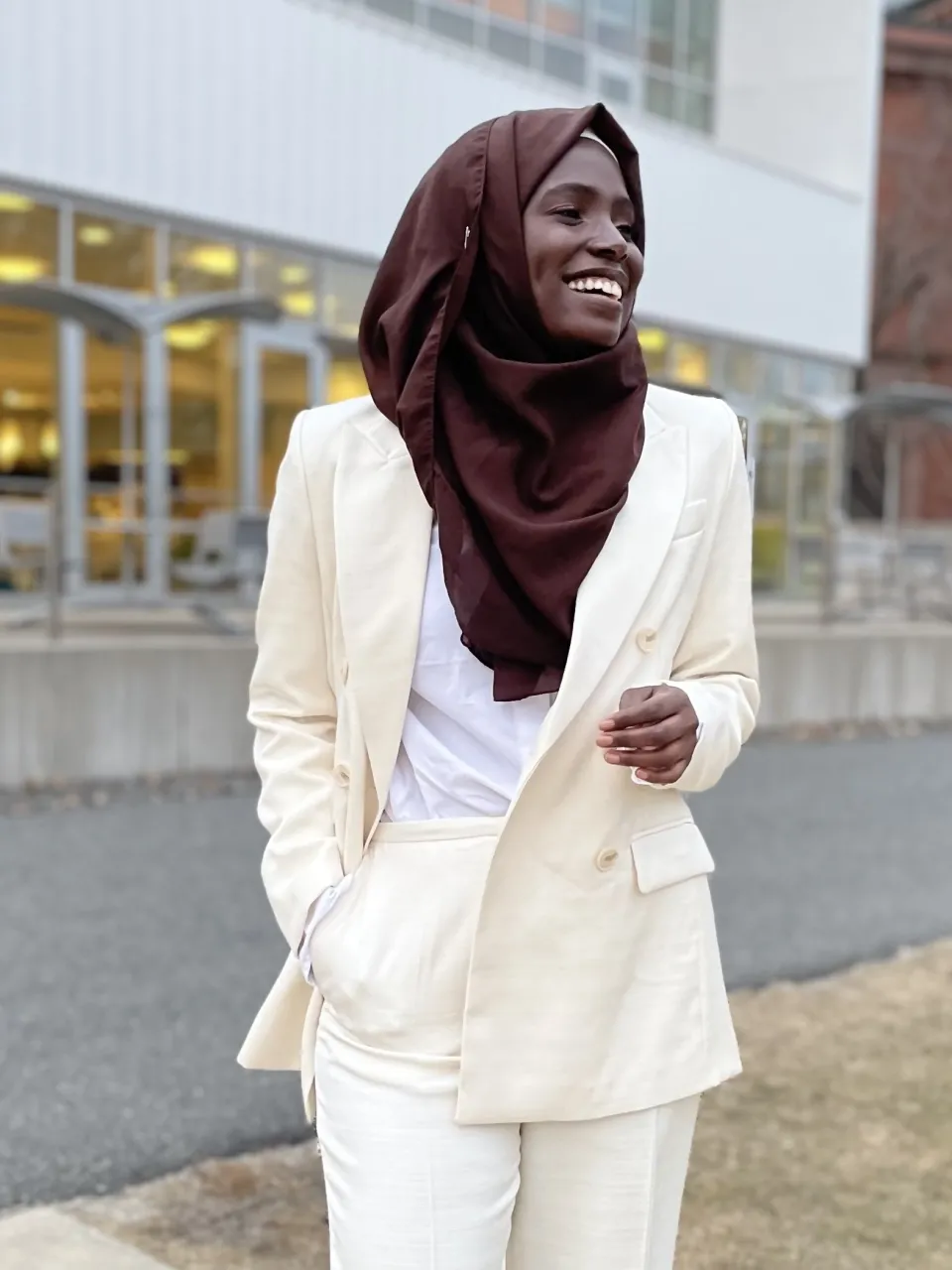 Hamssatou Almahamoudou Maiga ‘24 laughing in a white suit in front of the campus center